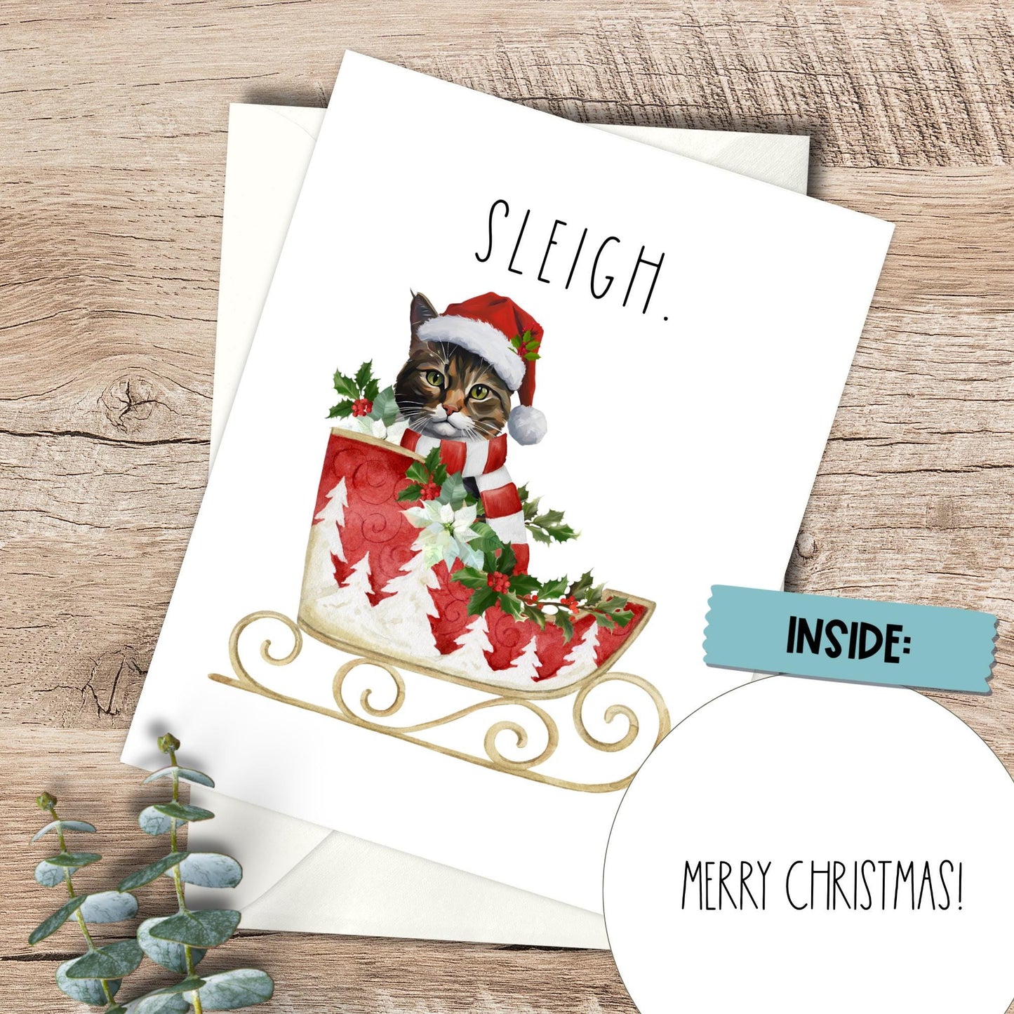 Christmas card with a cat in a Santa hat and sleigh on a wooden surface.