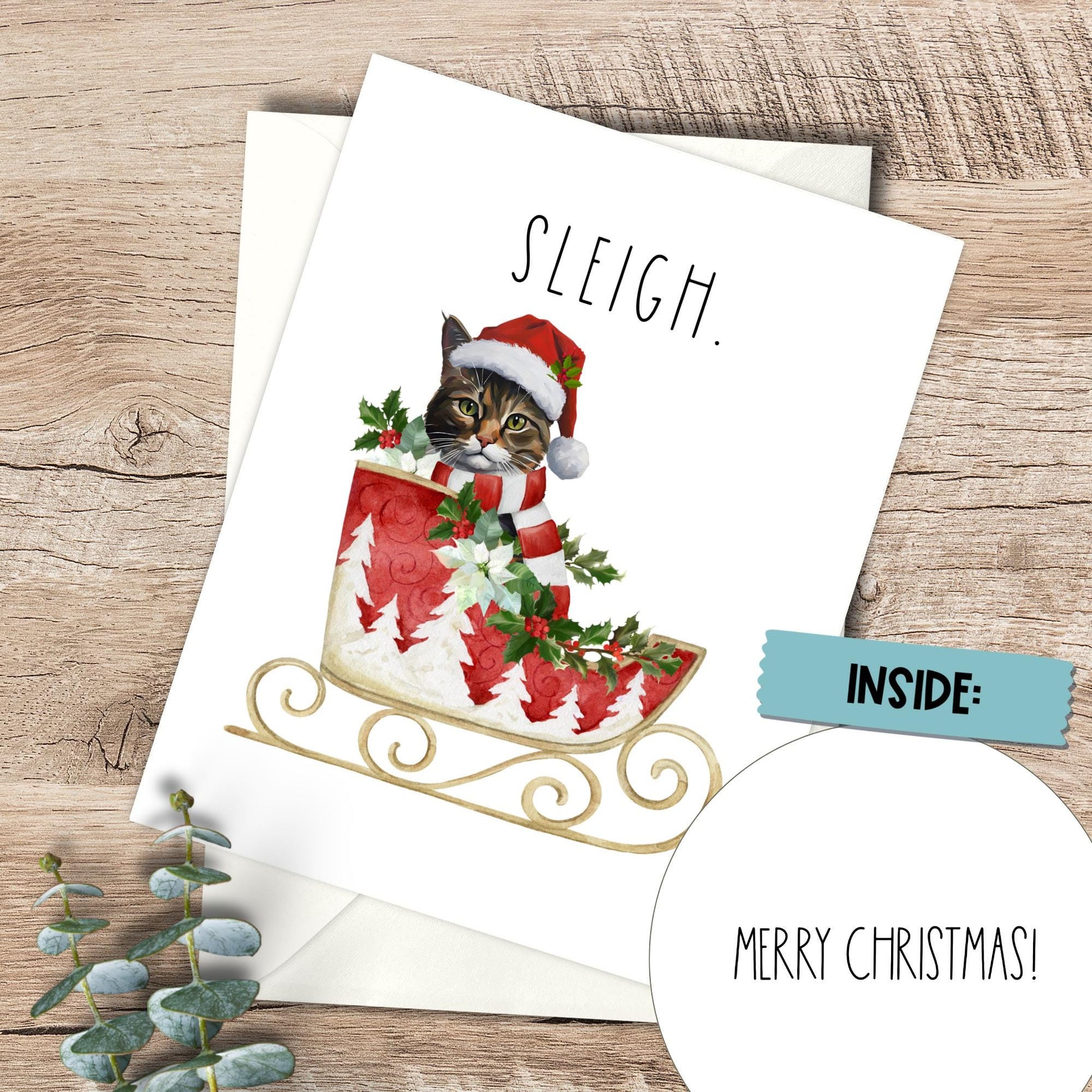 Christmas card with a cat in a Santa hat and sleigh on a wooden surface.