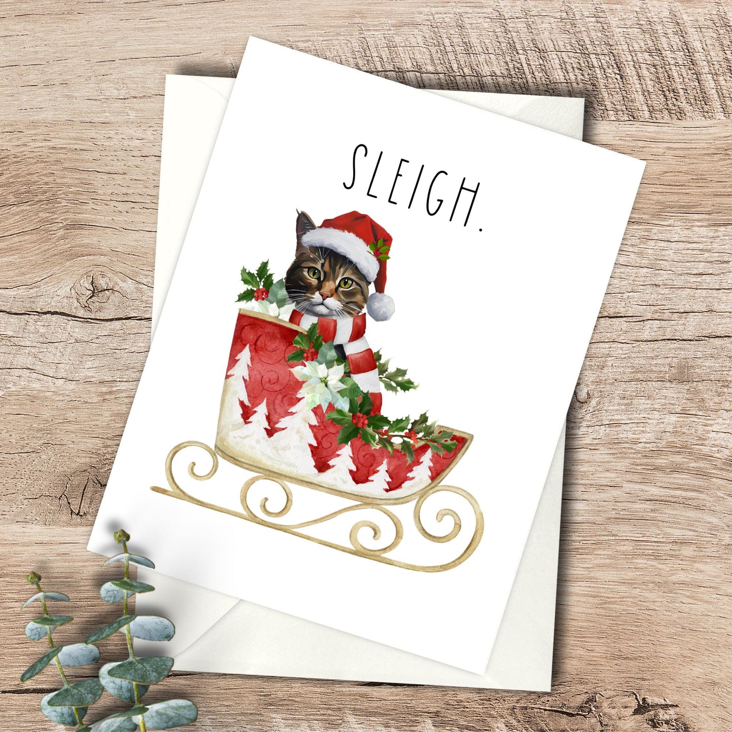 Christmas card with a cat in a Santa hat and sleigh on a wooden surface